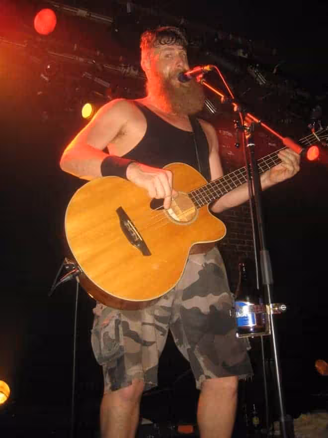 Un homme barbu se produisant lors d'un concert de Hayseed Dixie, jouant d'une guitare acoustique.
