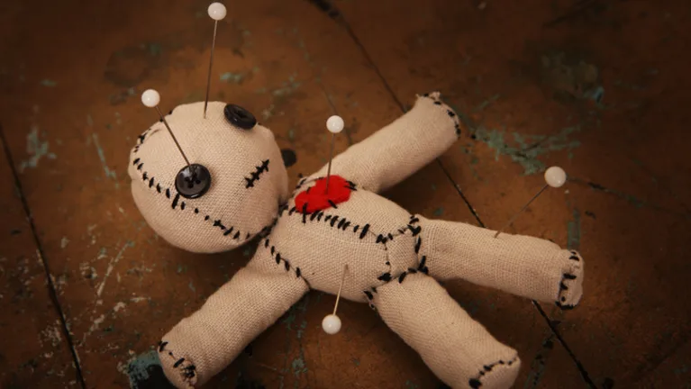 A voodoo doll with pins laying on a wooden floor.