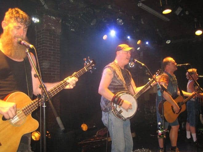 Le groupe Hayseed Dixie donne un concert animé sur scène à la Maroquinerie, avec des hommes jouant des banjos et des guitares.